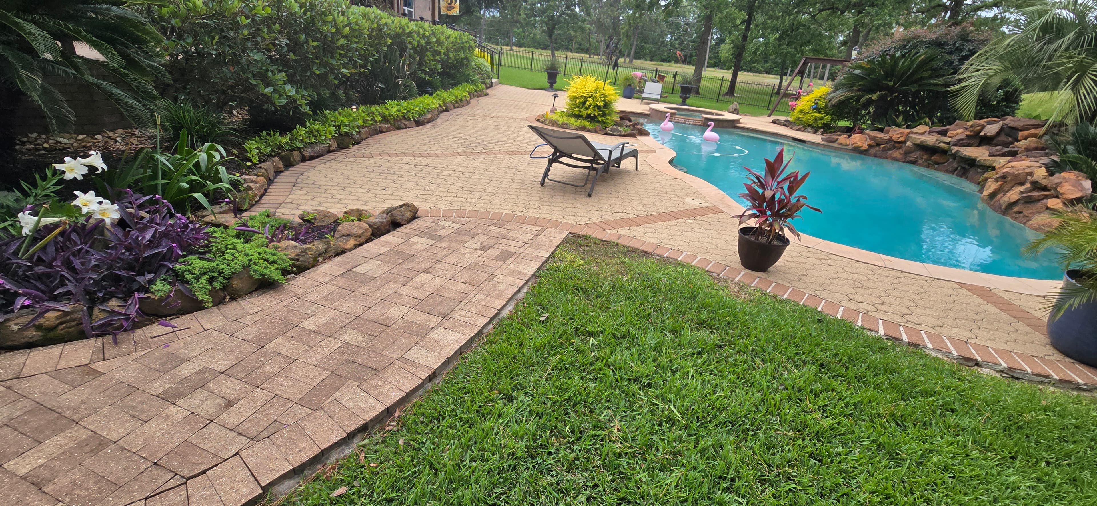 Backyard swimming pool with pink flamingo floats, brick patio, lounge chair, and lush landscaping.
