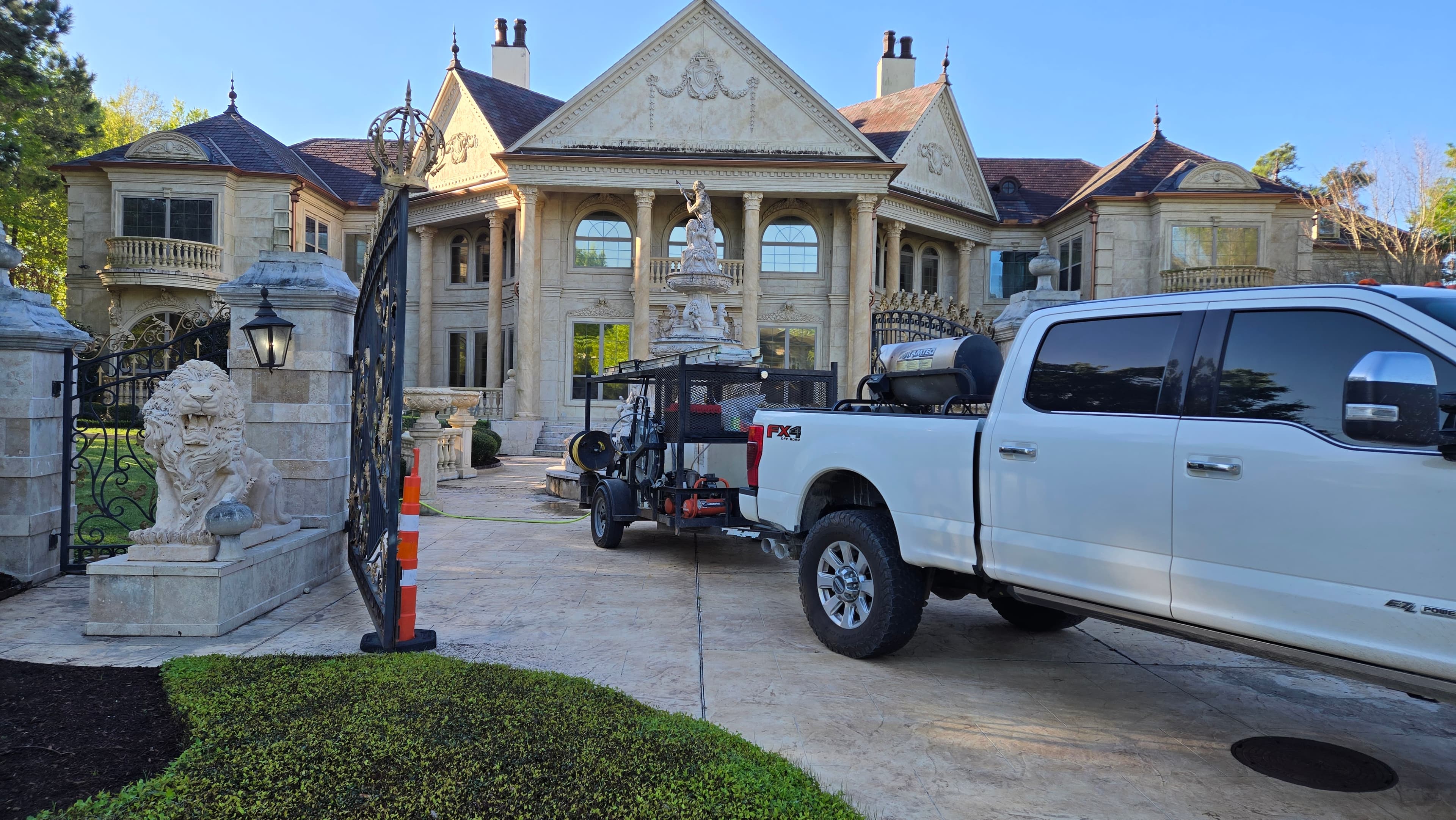 White pickup truck with trailer parked in front of a grand, classical-style stone mansion.