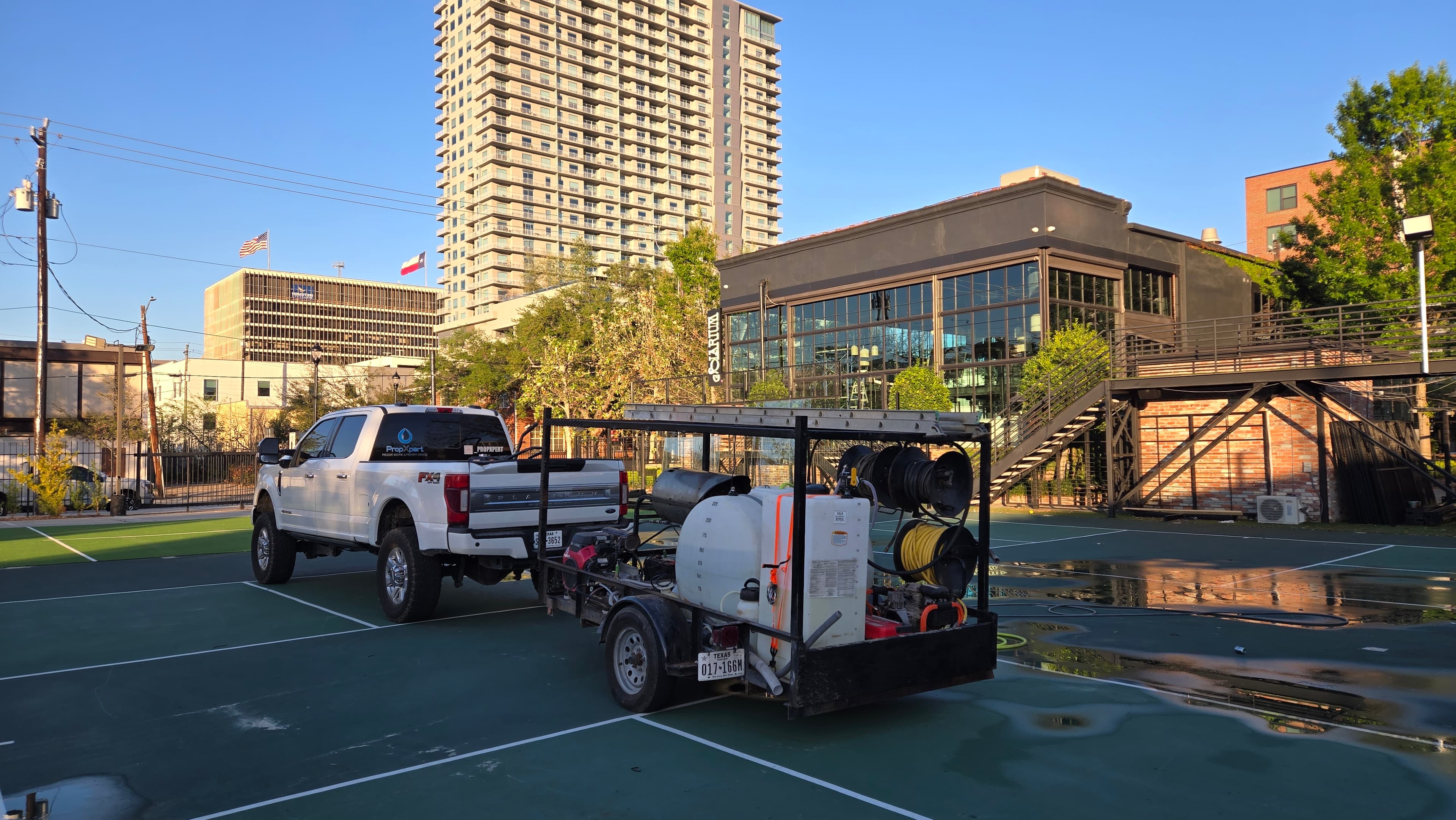 White pickup truck towing a pressure washing trailer on a wet outdoor sports court.