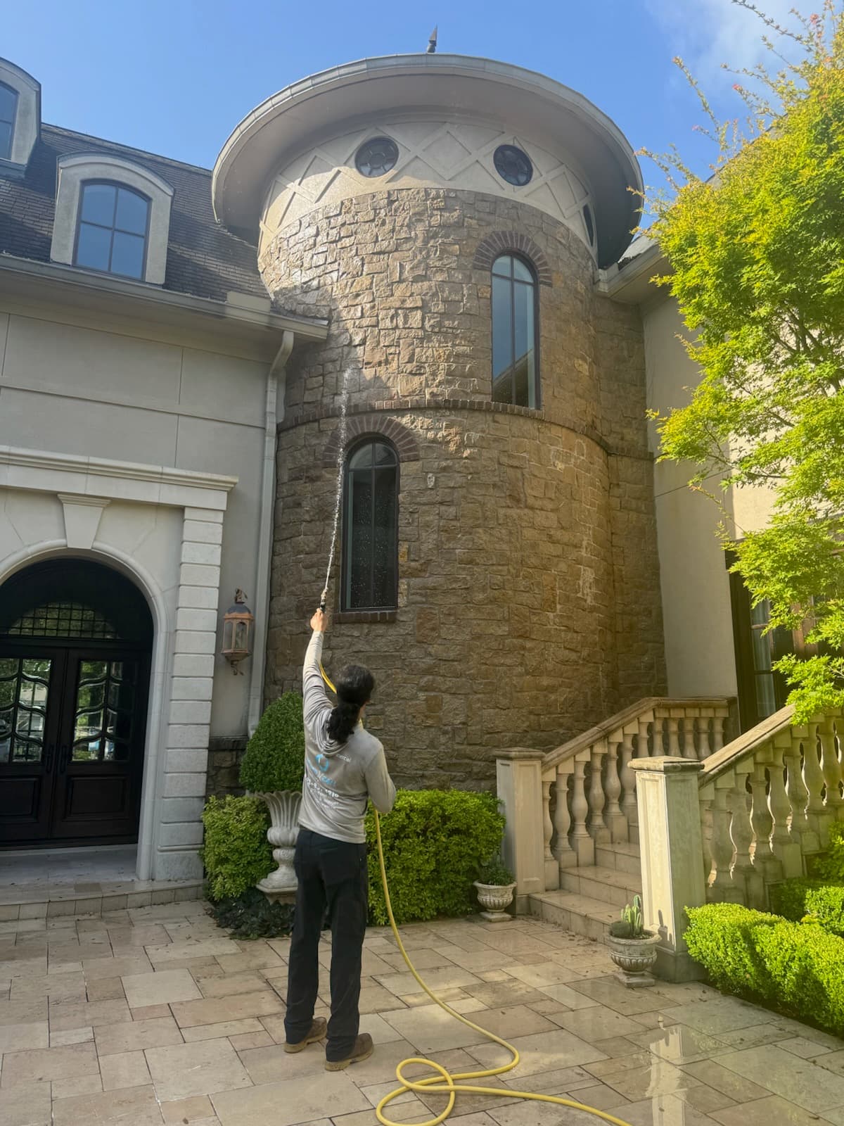 A person power washing the stone turret of a large house with a high-pressure hose.