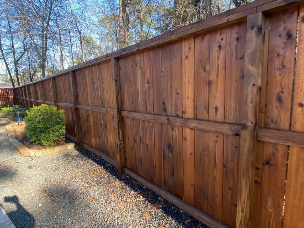 Dark stained wooden privacy fence with vertical planks and horizontal rails bordering a gravel yard.